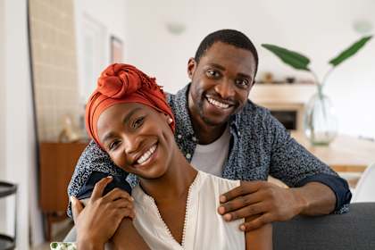 A man and woman are sitting closely together, with the woman's arm around the man's shoulder.