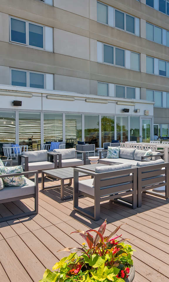 A wooden deck with chairs and tables is in front of a building.