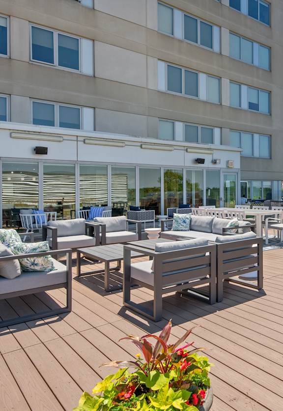 A wooden deck with chairs and tables is in front of a building.