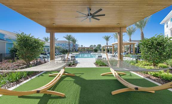 A wooden pergola with a ceiling fan is over a green lawn with two hammocks.at Allegra at Cocoa in Cocoa, FL, 32926