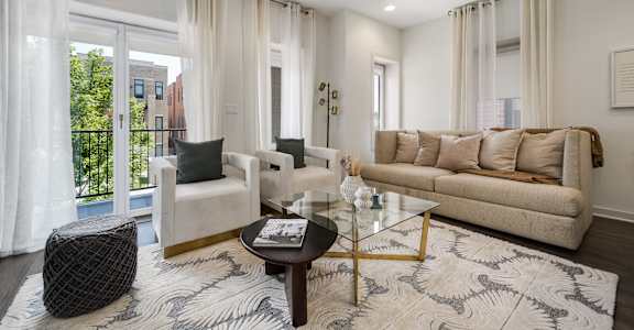 A living room with a white sofa, a black ottoman, and a glass coffee table.