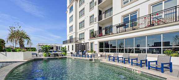 Our swimming pool in on the rooftop patio with blue chairs around it at Dominion Post Oak apartments in Houston, TX