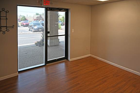 A room with a wooden floor and a door leading to a street.