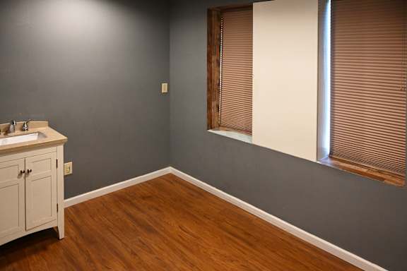 A kitchen with a wooden floor and a window with blinds.
