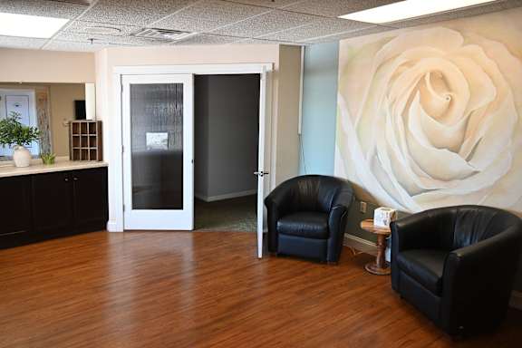 Two black chairs are placed in front of a large white rose on the wall.