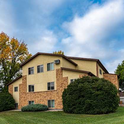 The view of an apartment building with green grass and trees. Fargo, ND Huntington Apartments.