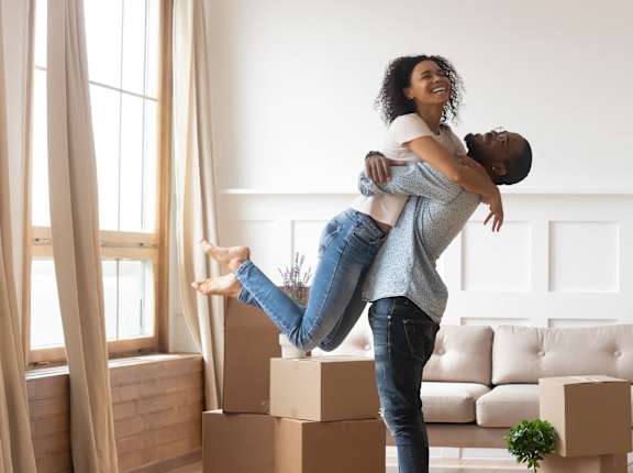 a woman holding a man in the air in a living room with boxes