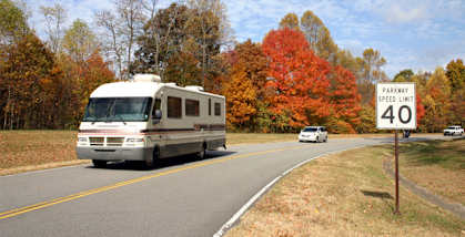 A parkway speed limit sign is posted on the side of a road with a motorhome driving by.