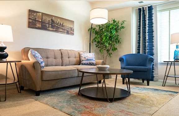 A living room with a beige couch, a blue chair, and a round coffee table.
