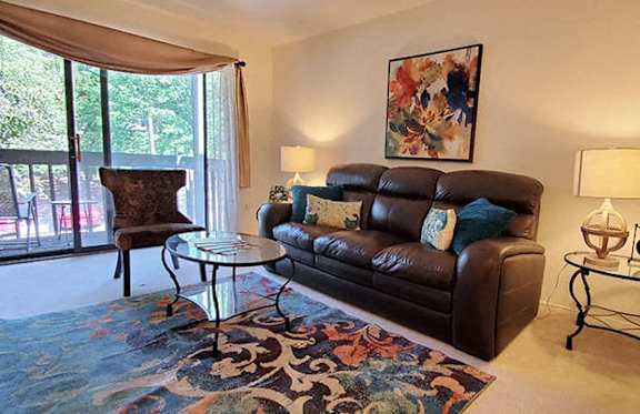 A living room with a brown leather couch, a glass table, and a floral rug.