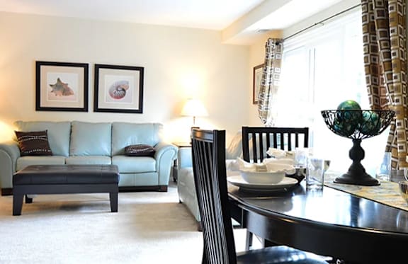 A living room with a blue couch, a black coffee table, and a dining table set for two.