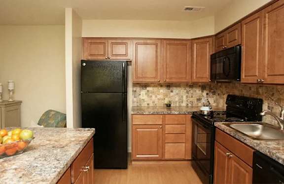 A kitchen with a black refrigerator and wooden cabinets.