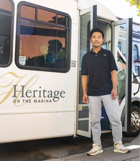 A man stands in front of a bus with the words "Heritage on the Marina" written on it.