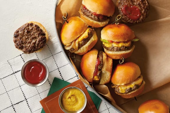 A tray of burgers with condiments on the side.