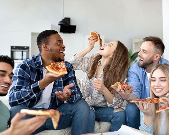 a group of people sitting on a couch eating pizza