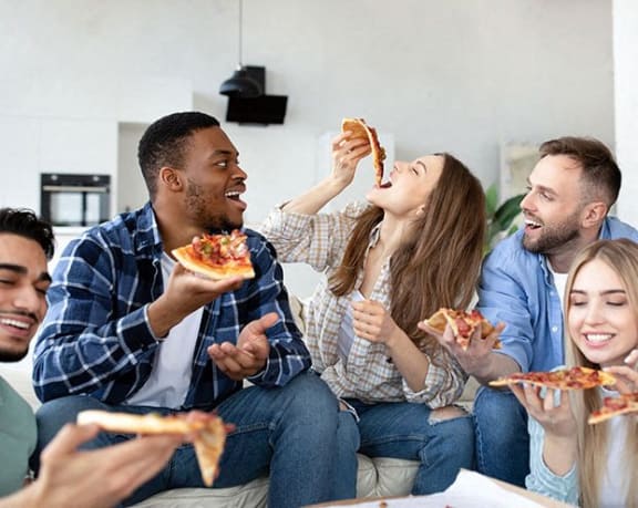 a group of people sitting on a couch eating pizza