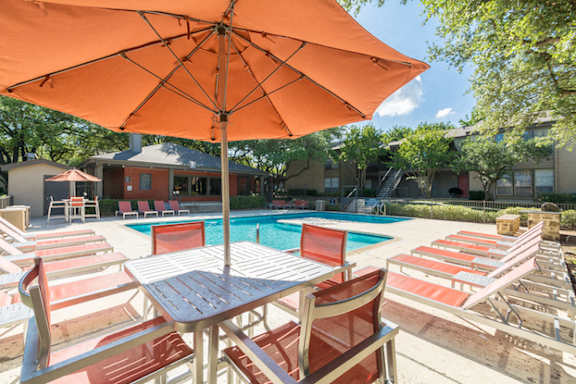 Swimming pool with striped lounge chairs under orange umbrella at The Colony Apartments, Texas, 78148