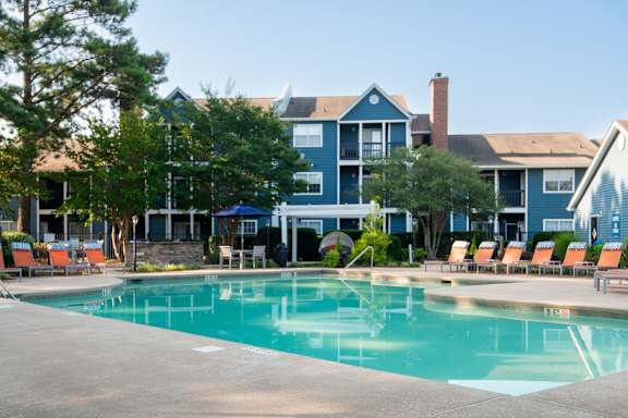 A swimming pool in front of a blue building with orange chairs around it.