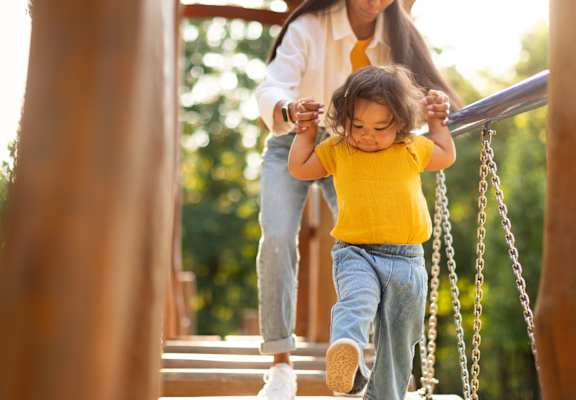 A child in a yellow shirt is walking on a swing set.