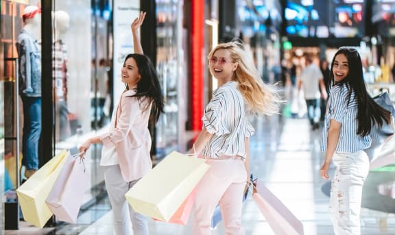 three women walking through a shopping mall holding shopping bags