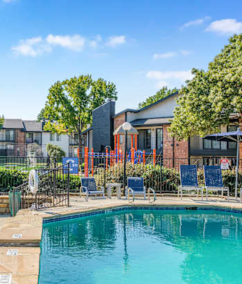 A swimming pool surrounded by lounge chairs and umbrellas with a building in the background. at Water Ridge Apartments , Texas, 75061