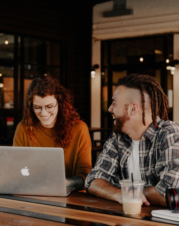 two people sitting at a table looking at a laptop