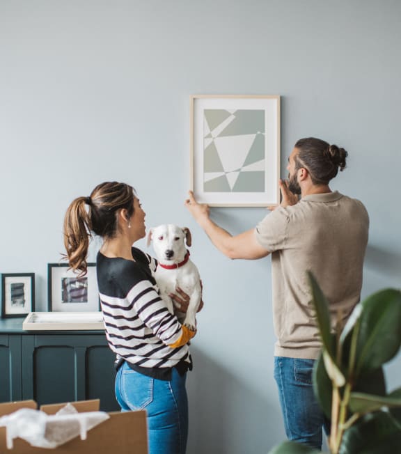 a man and woman holding a dog looking at a picture on a wall