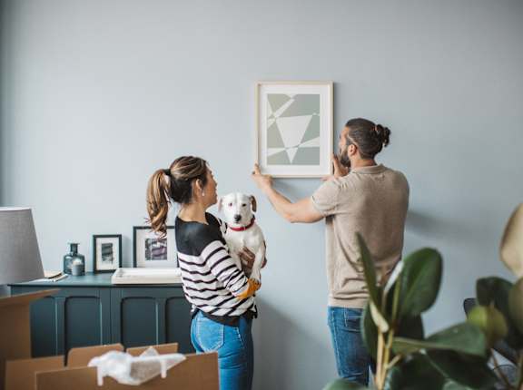 a man and woman holding a dog looking at a picture on a wall
