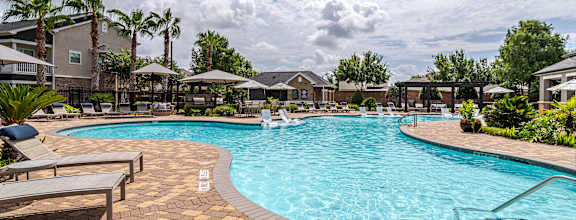 A large outdoor swimming pool surrounded by a brick patio and lounge chairs at Avenues at Shadow Creek Ranch Apartments, Pearland, TX