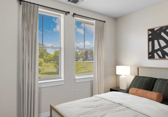 a bedroom with a bed and three windows with white curtains at Rosemont Square in Massachusetts 02368