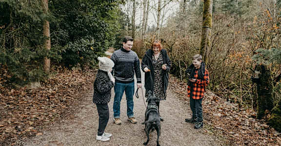 A family of four walking their dog in the woods.