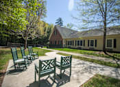 Thumbnail 29 of 31 - A sunny day at a park with a bench and a building in the background.