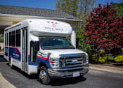 Thumbnail 31 of 31 - A white bus with blue and red stripes is parked in front of a building.