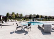 Thumbnail 2 of 11 - A poolside table and chairs are arranged on a patio.