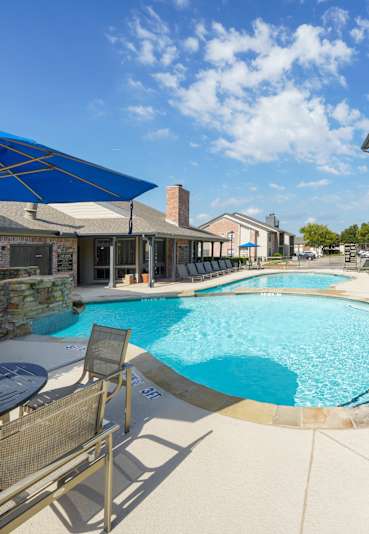 A pool surrounded by a concrete patio and a blue umbrella.