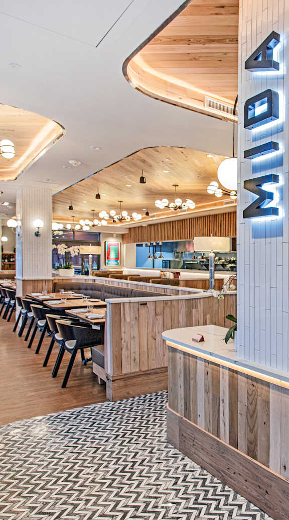 A modern restaurant interior with wooden elements and a central bar area. at Trio Newton Apartments, Massachusetts, 02460