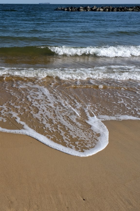 a beach with a body of water and a wave on the sand at The Port at East Beach Apartments and Marina, Virginia