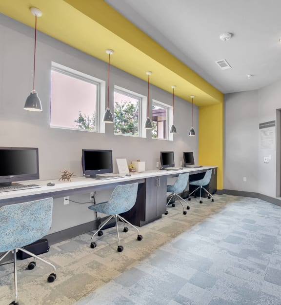 a long desk with computers and chairs in a room with a yellow wall