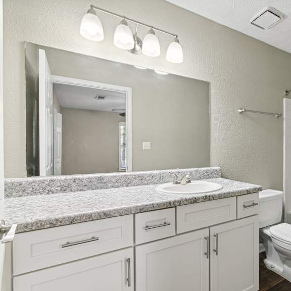 A white bathroom with a marble countertop and a white toilet.