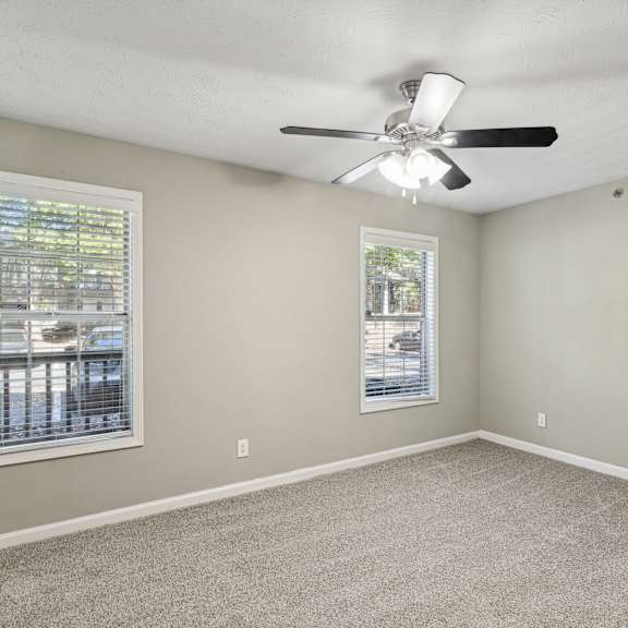 A room with a ceiling fan and two windows.