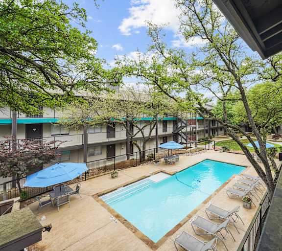 A pool surrounded by chairs and trees.
