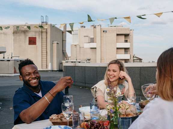 Three people are sitting at a table with food and drinks, enjoying a meal together.