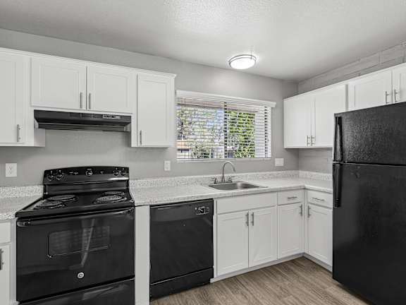 A black refrigerator stands in a kitchen with white cabinets and a black stove.