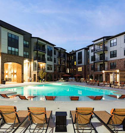 an apartment swimming pool at night with chairs around it