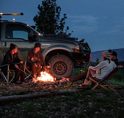 a group of people sitting around a campfire next to a truck