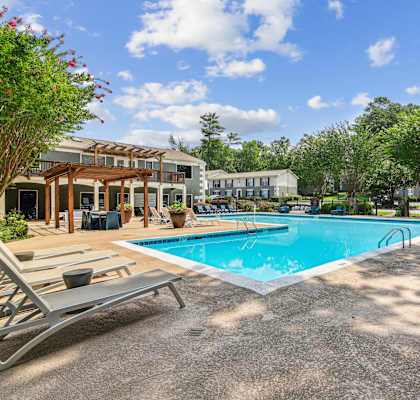 A pool area with sun loungers and a building in the background.