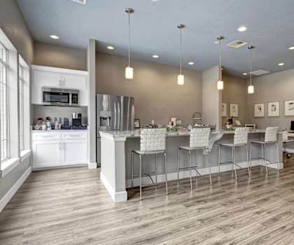 The community kitchen with a coffee machine, toaster, fridge, marble counters, and barstool chairs and a small business center with a desktop computer at Harbin Pointe Apartment Homes. 
