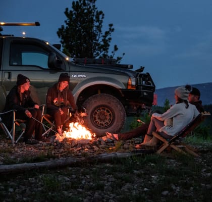 a group of people sitting around a campfire next to a truck