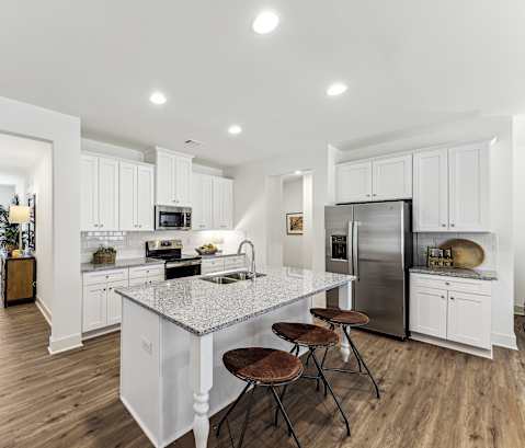 a white kitchen with a marble counter top and a stainless steel refrigerator