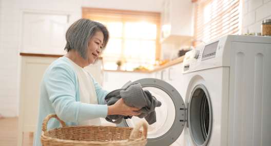 A woman is doing laundry by putting clothes into a washing machine.
